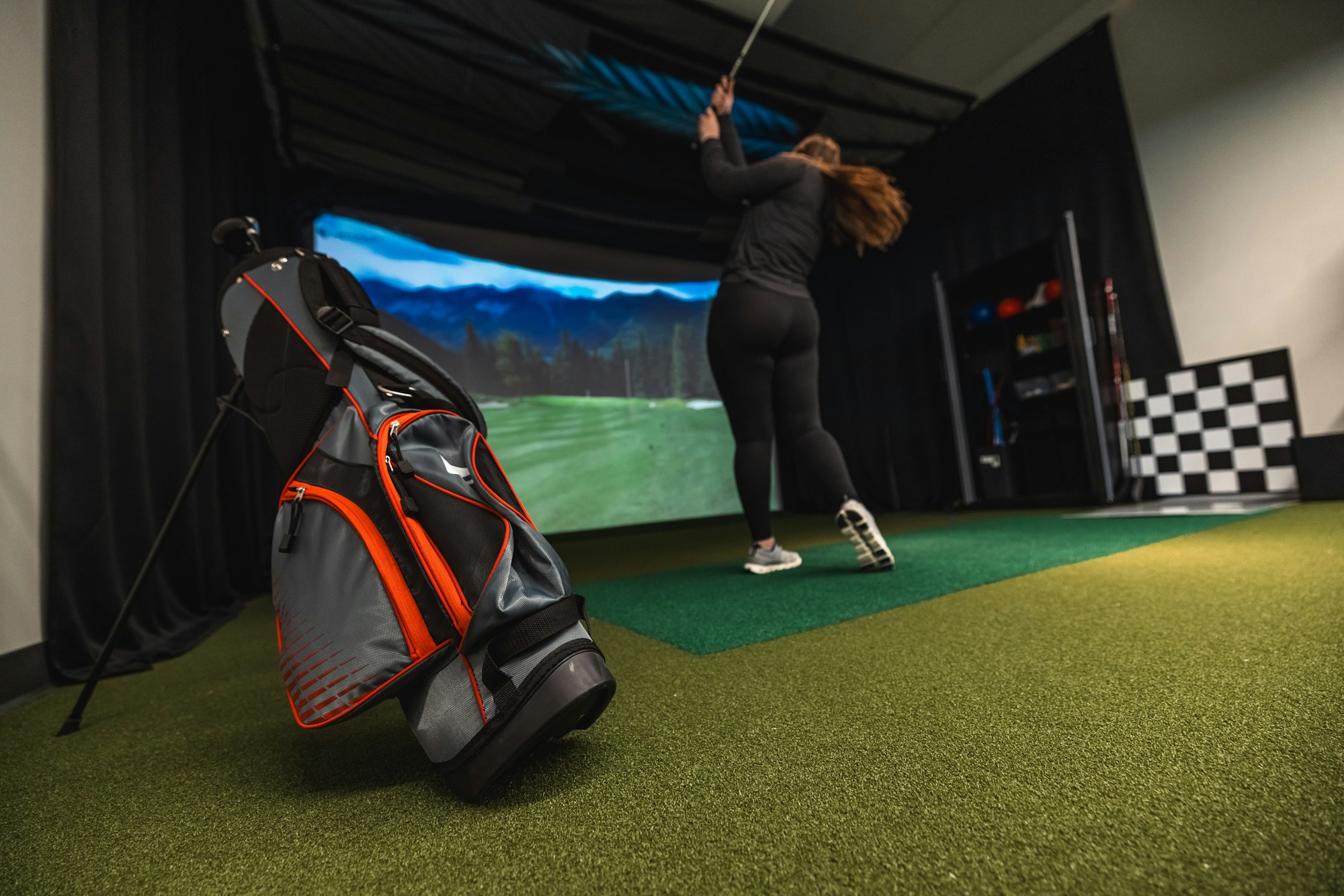 A person practicing golf in a simulator with a golf bag in the foreground.