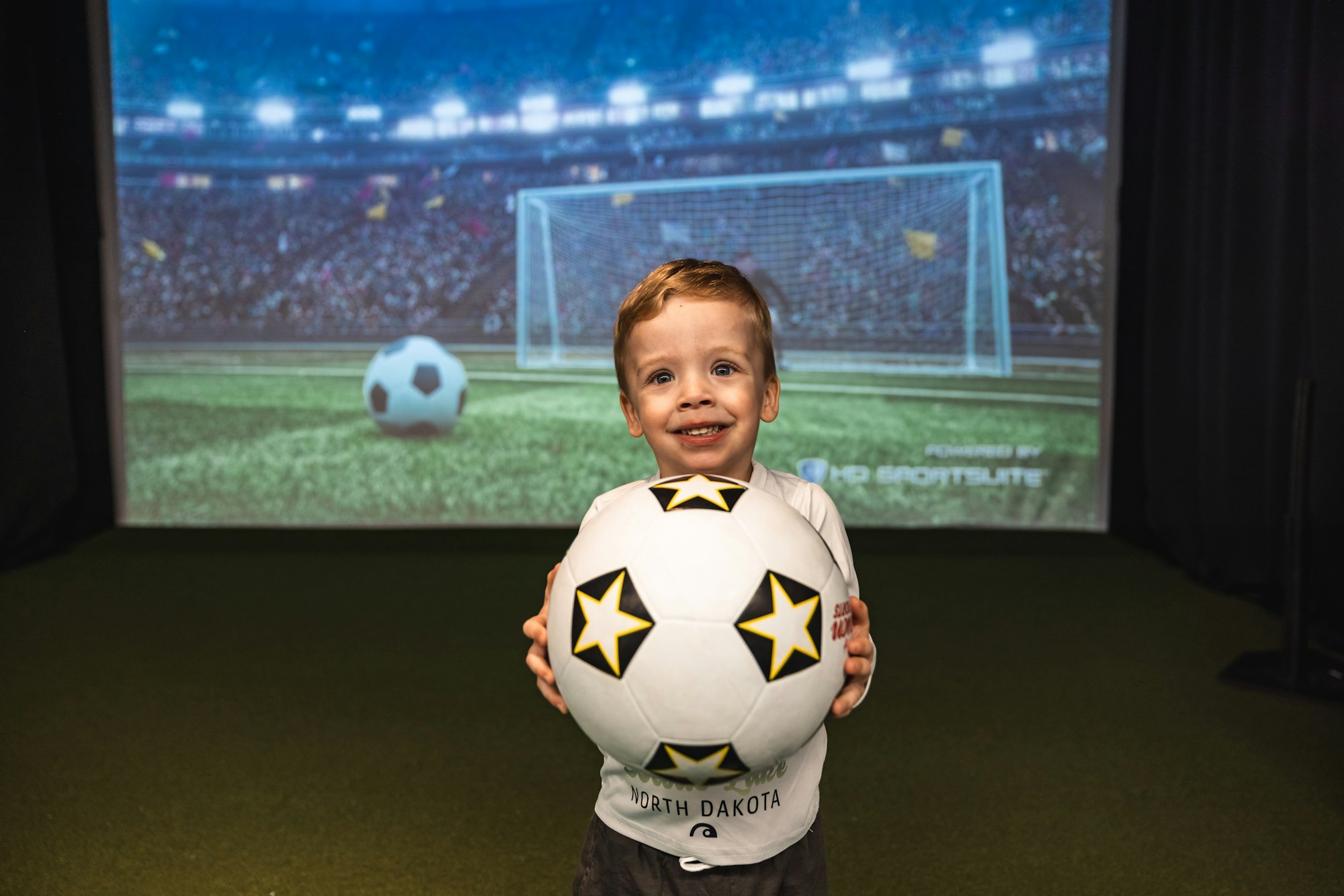 A smiling child holding a soccer ball with a stadium background.