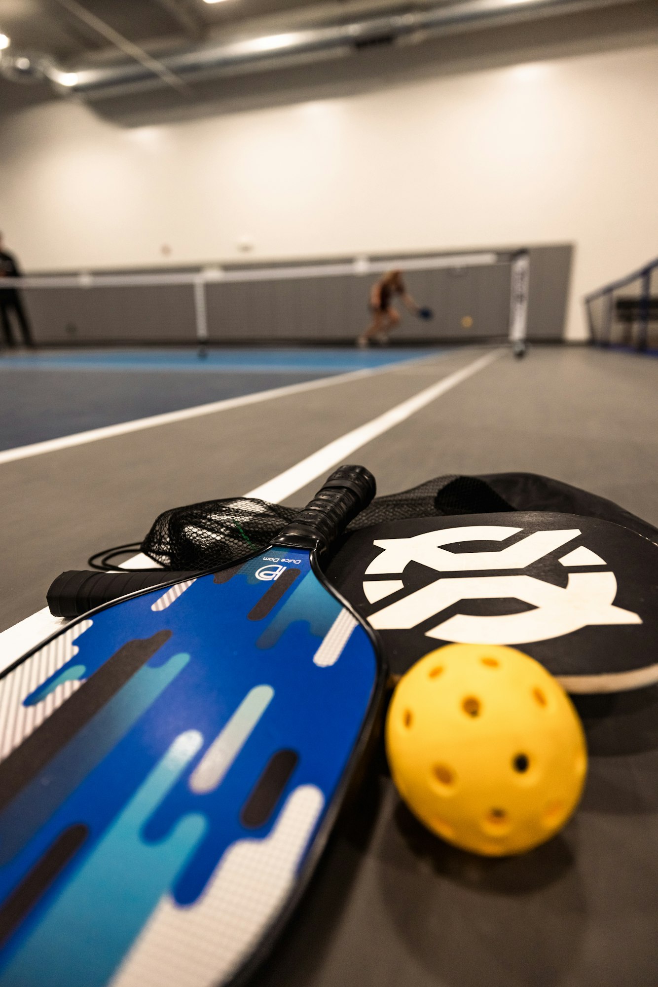 Pickleball paddles and ball, with out-of-focus player in background.