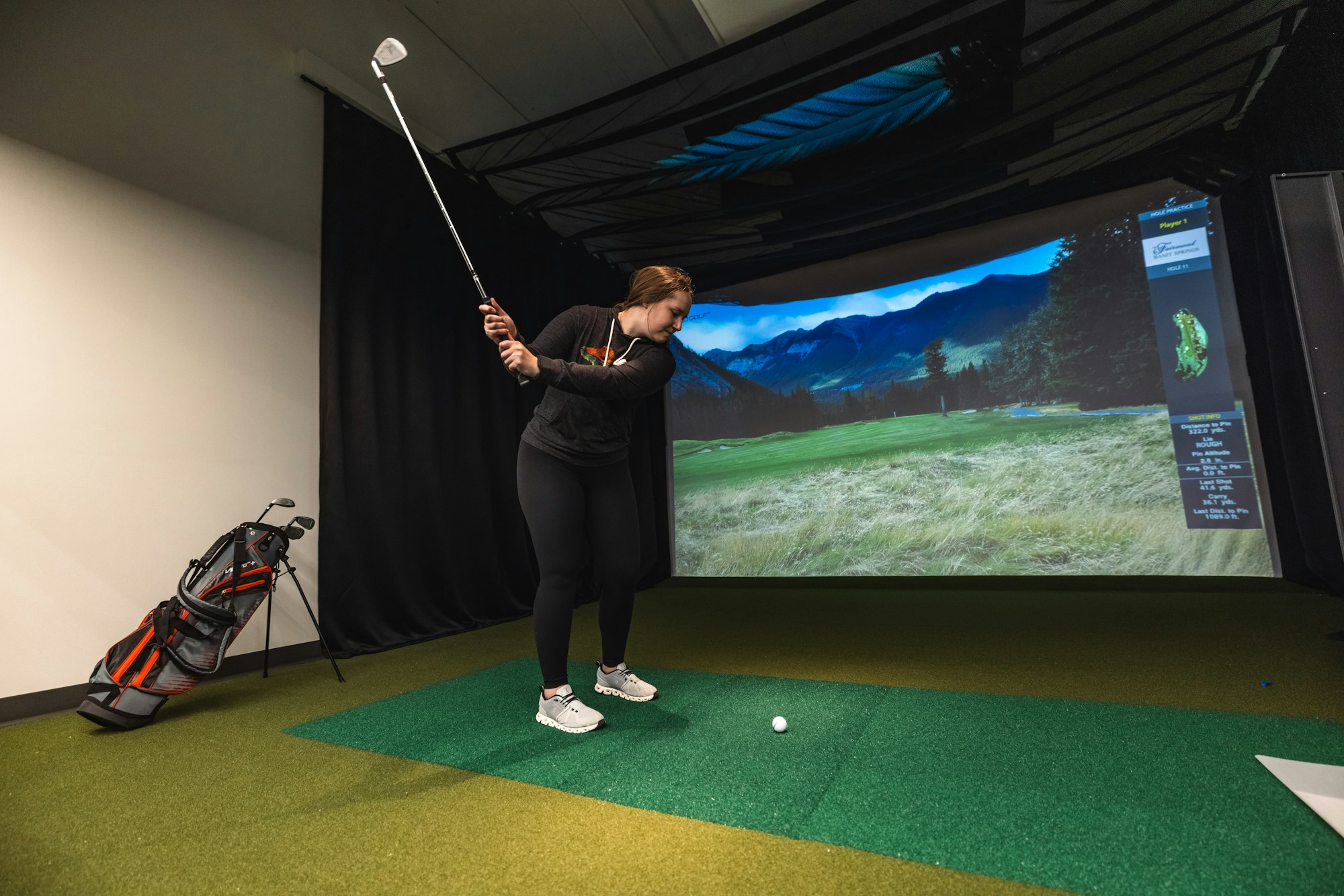 A person playing golf on a simulator indoors, with a virtual course displayed on the screen ahead.