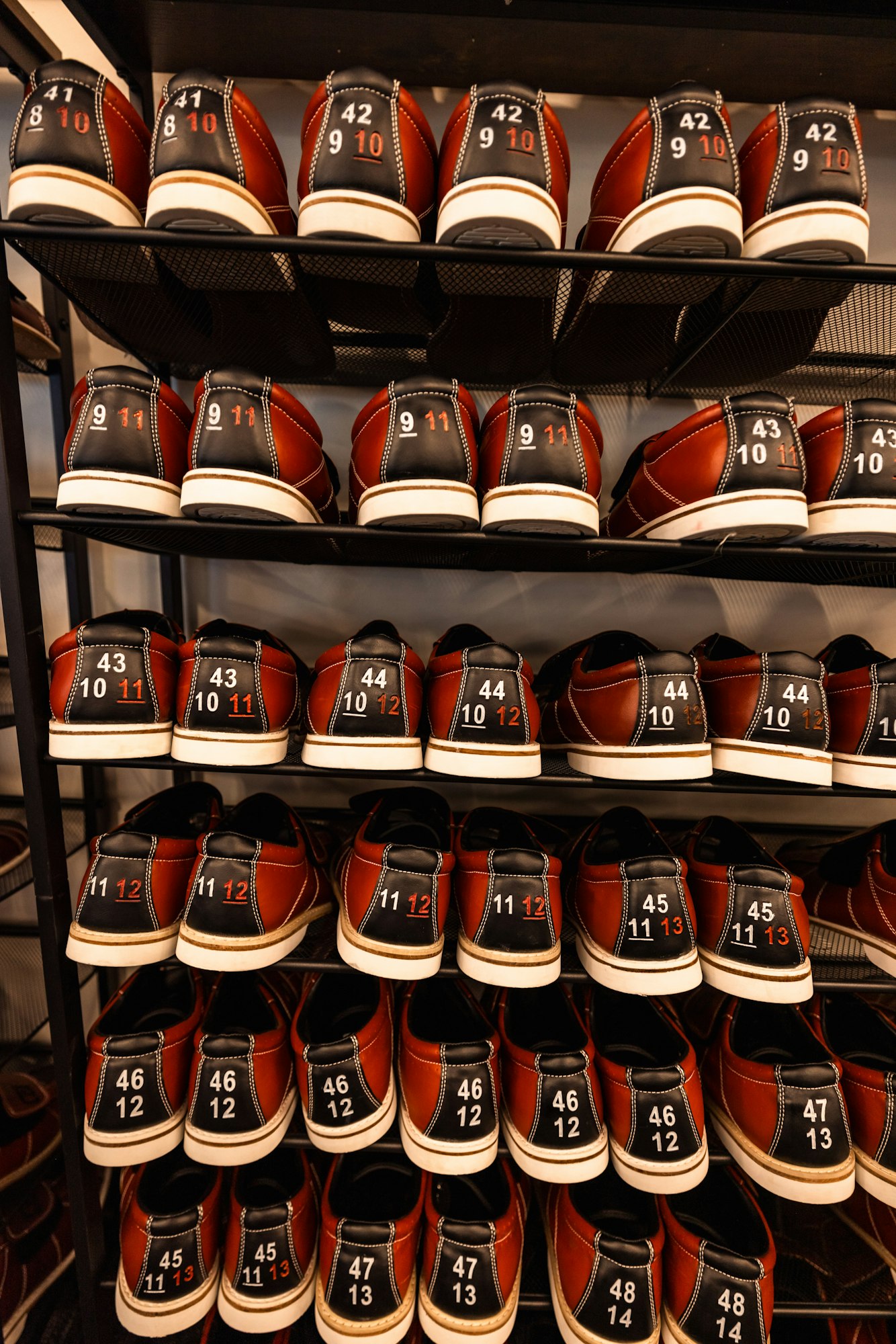 Rows of bowling shoes on shelves, marked with sizes.