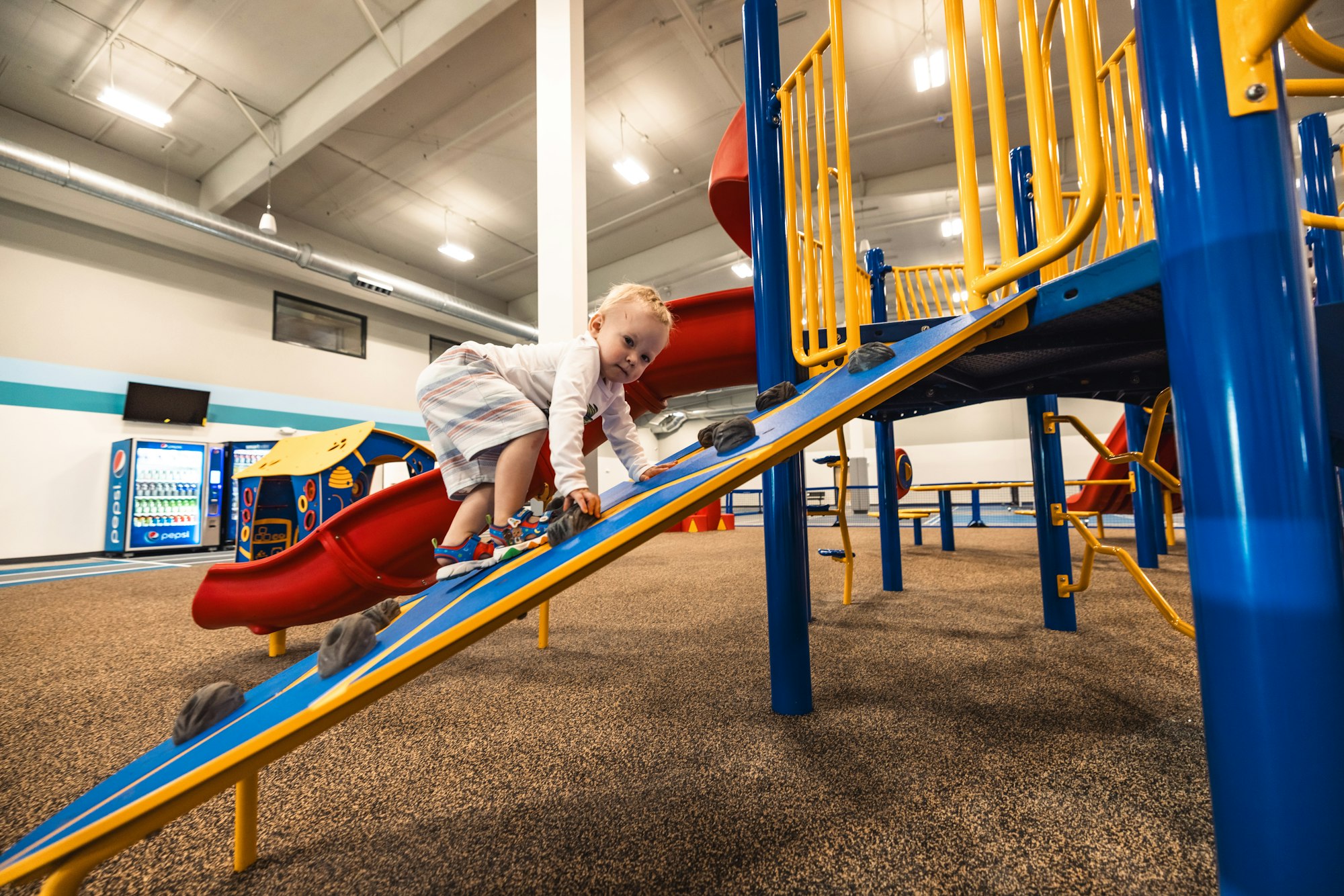 Child climbing down a red slide in an indoor play area.