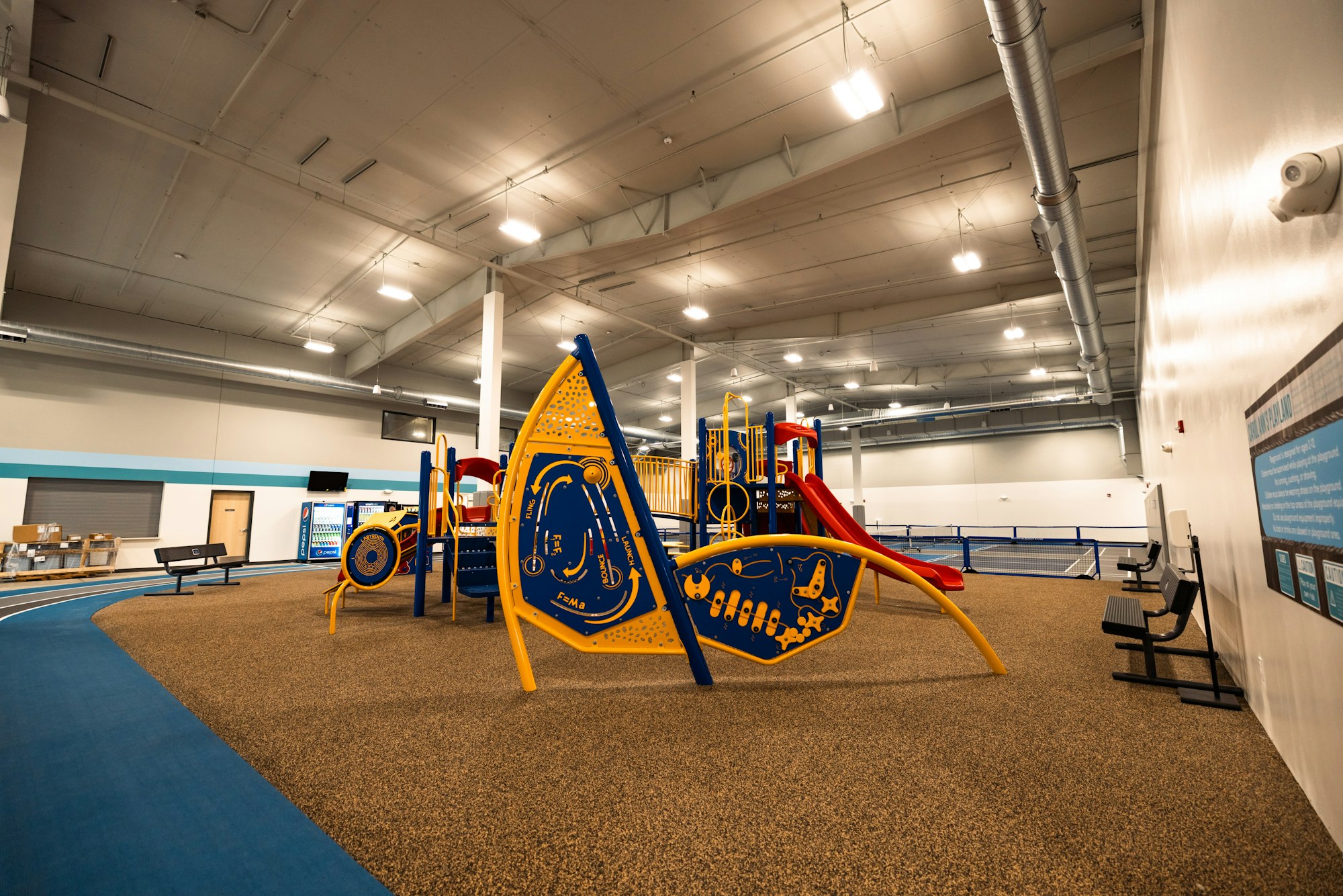 Indoor playground with colorful equipment, safety flooring, benches, and educational boards.