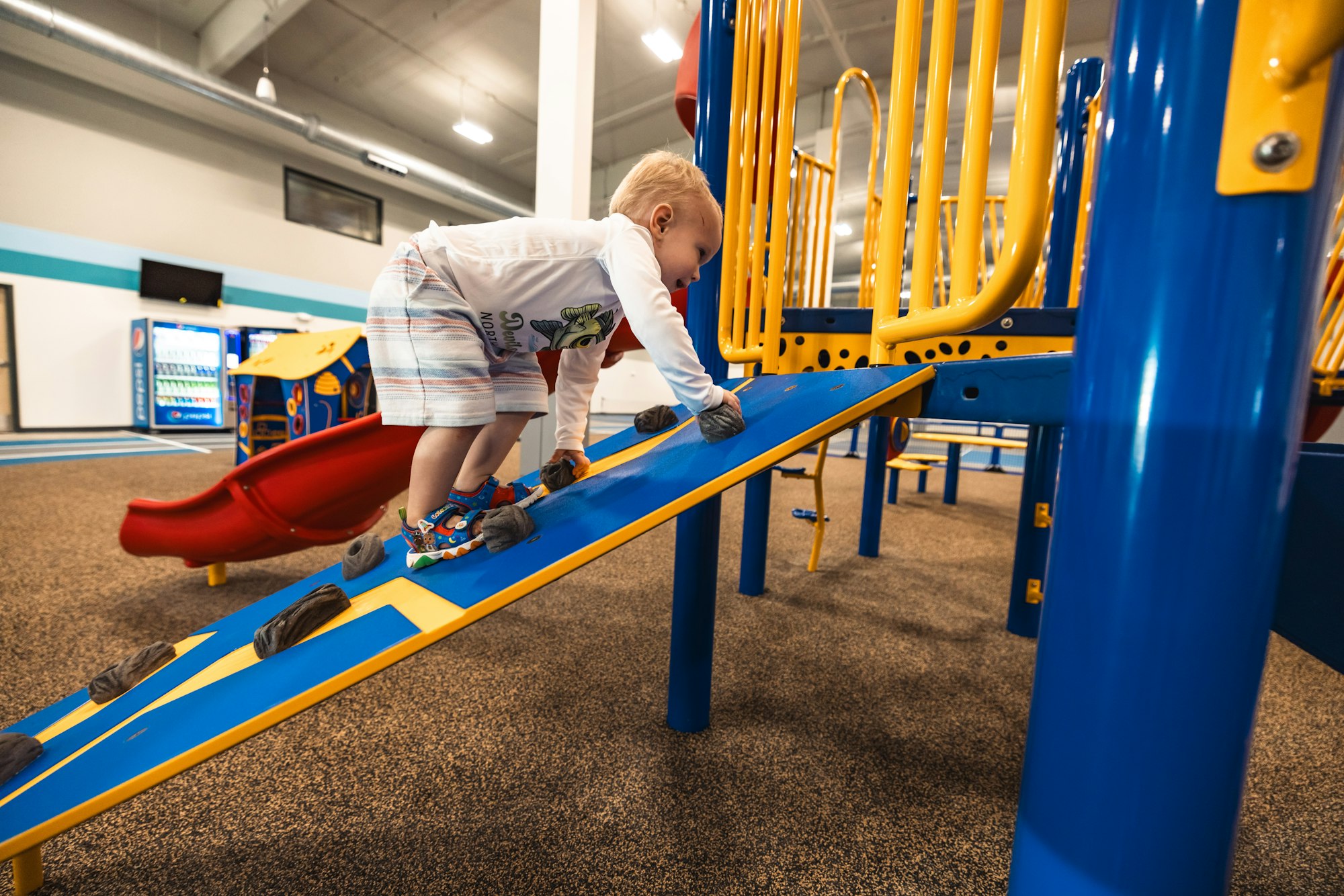 A child climbs a colorful playground structure indoors.