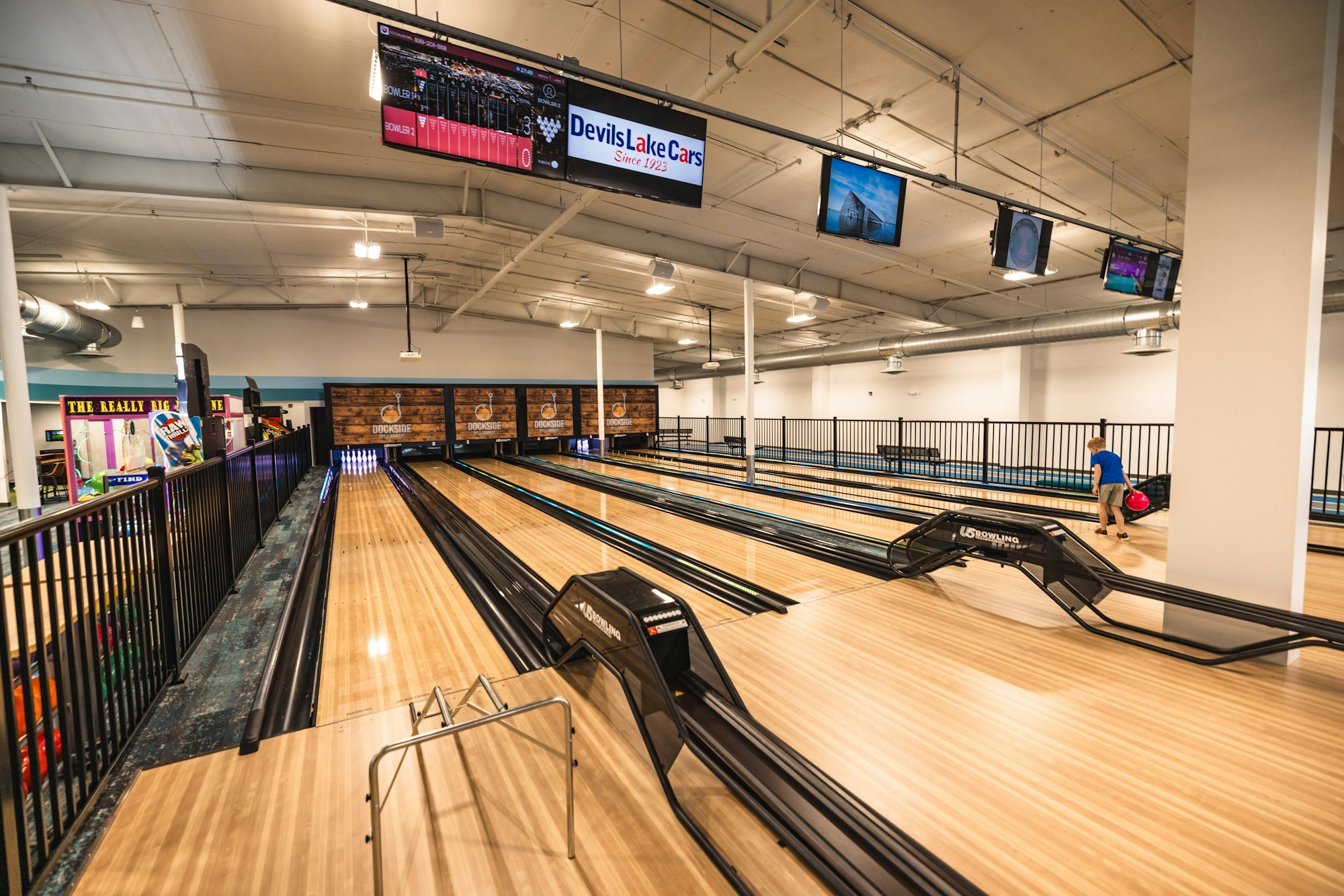 Indoor bowling alley with multiple lanes, screens displaying scores, and a person ready to bowl.