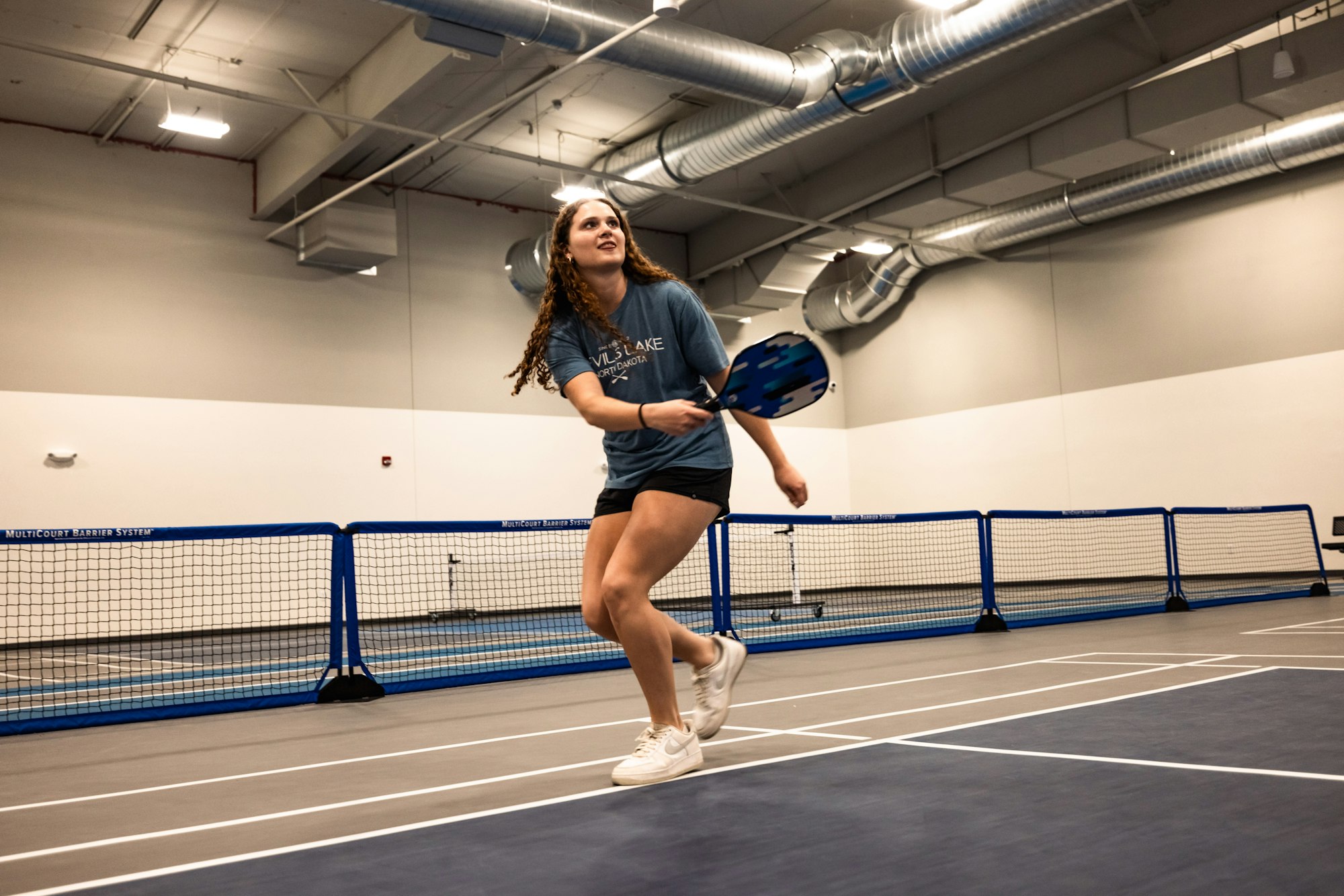 A woman playing pickleball indoors, focusing intently on the game.