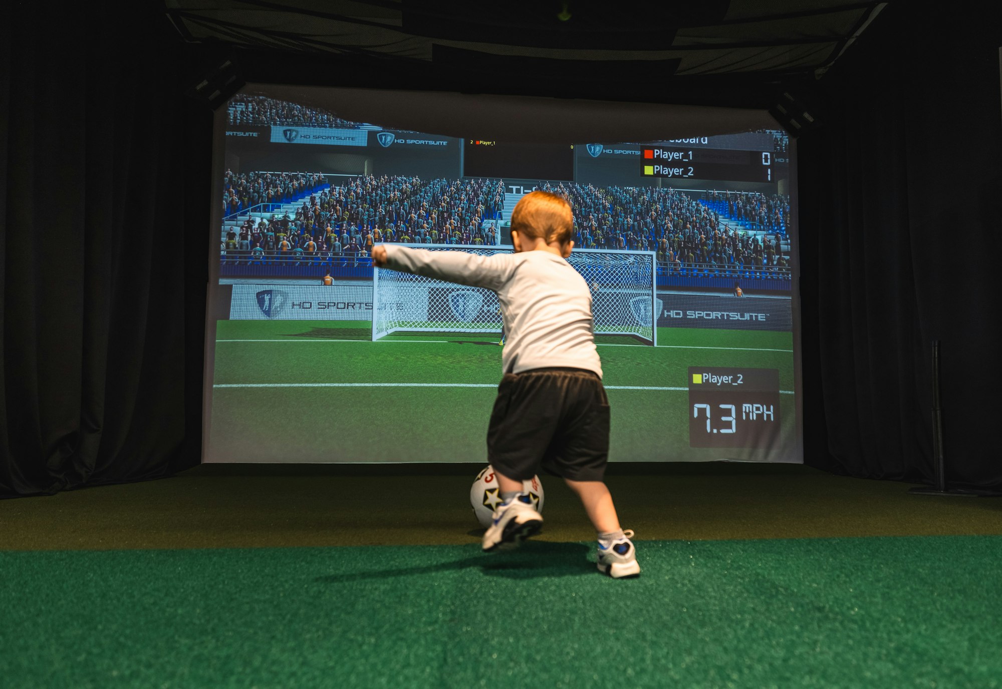 A child playing virtual soccer with a large projected screen showing the game.