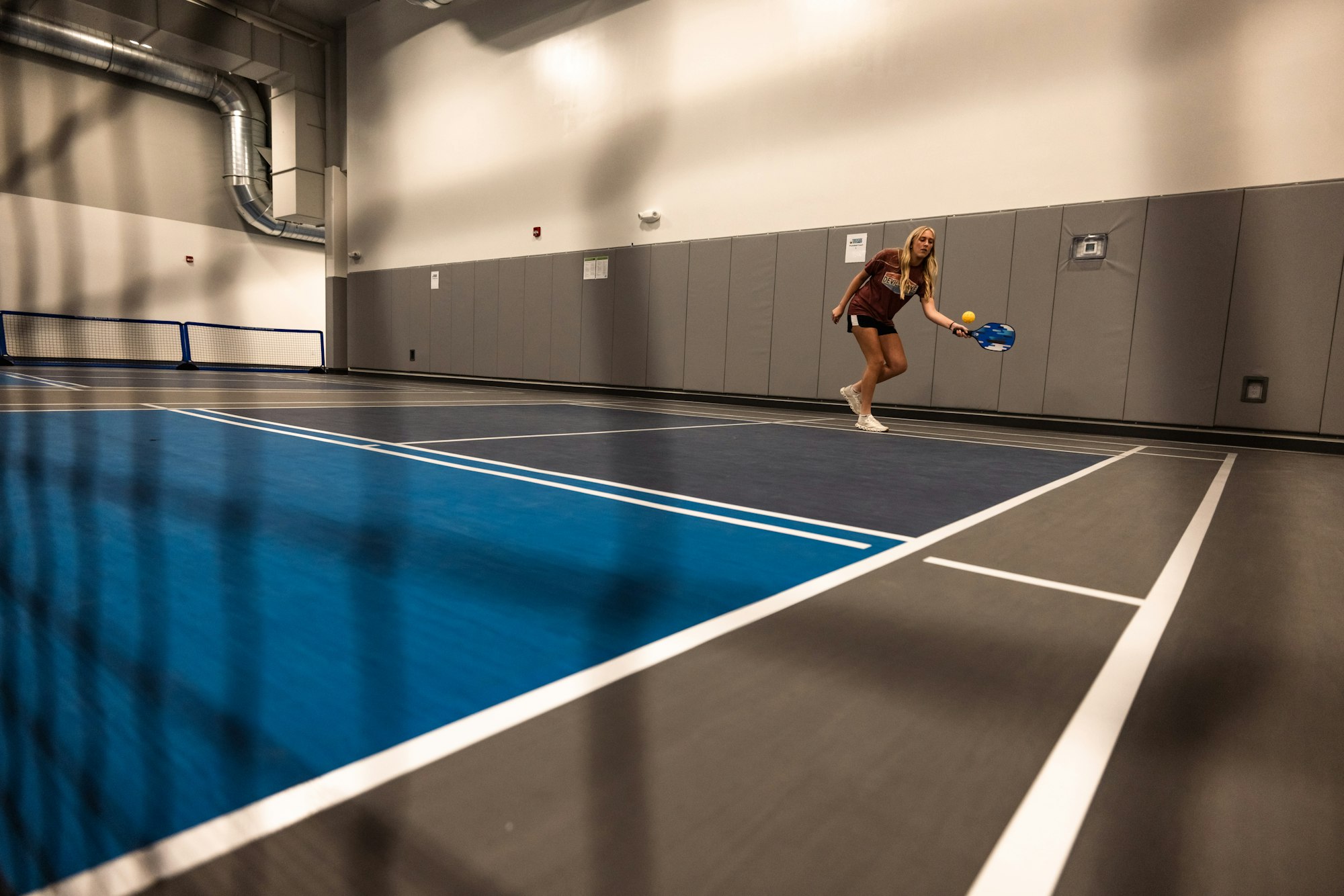 A person playing pickleball indoors on a blue court.