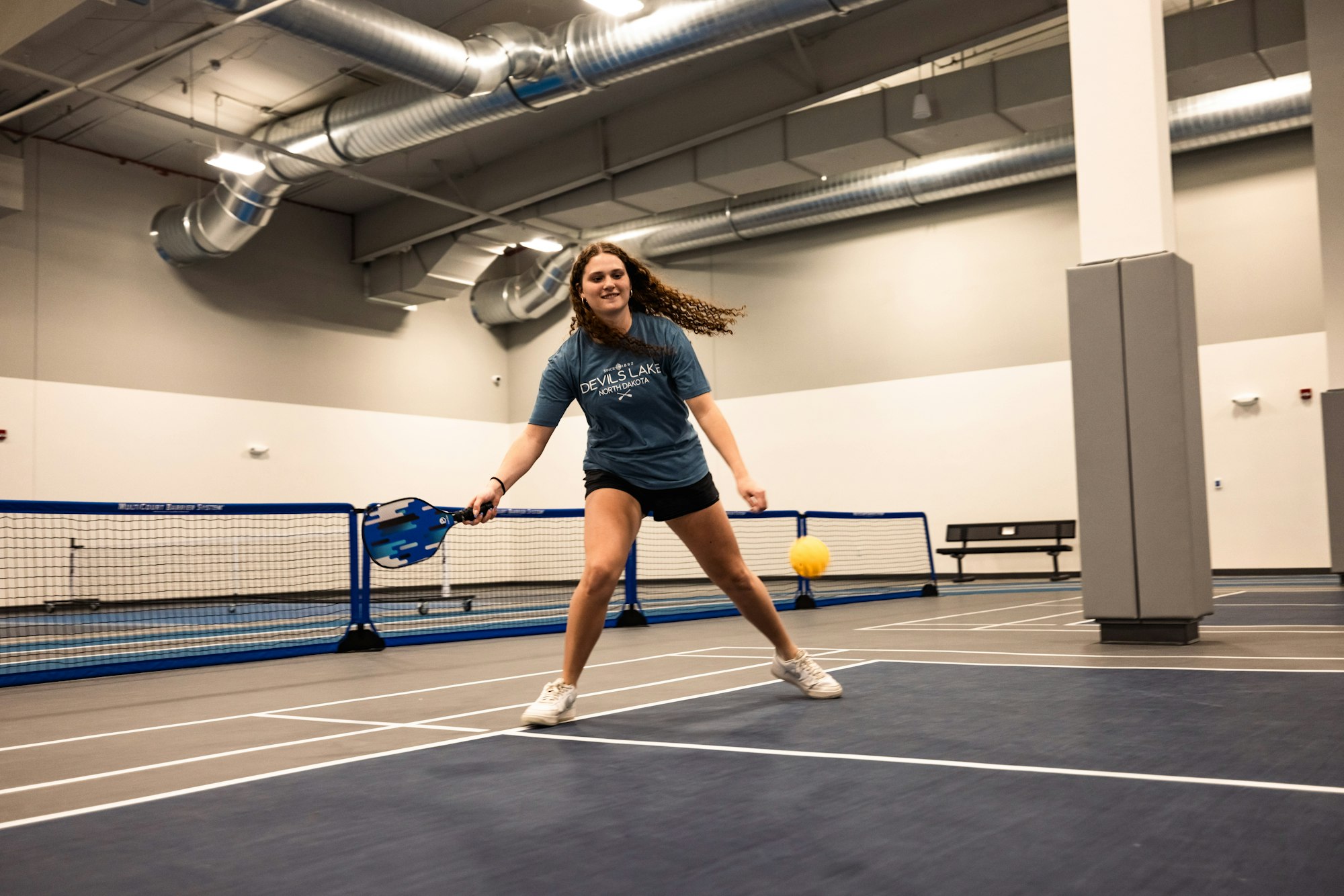A person playing pickleball indoors, poised to hit a yellow ball.