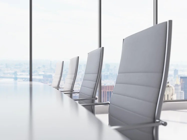Row of modern chairs in a conference room with cityscape view through floor-to-ceiling windows.