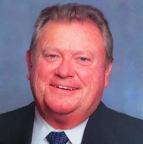 A smiling man with a blue tie and suit jacket against a blue background.