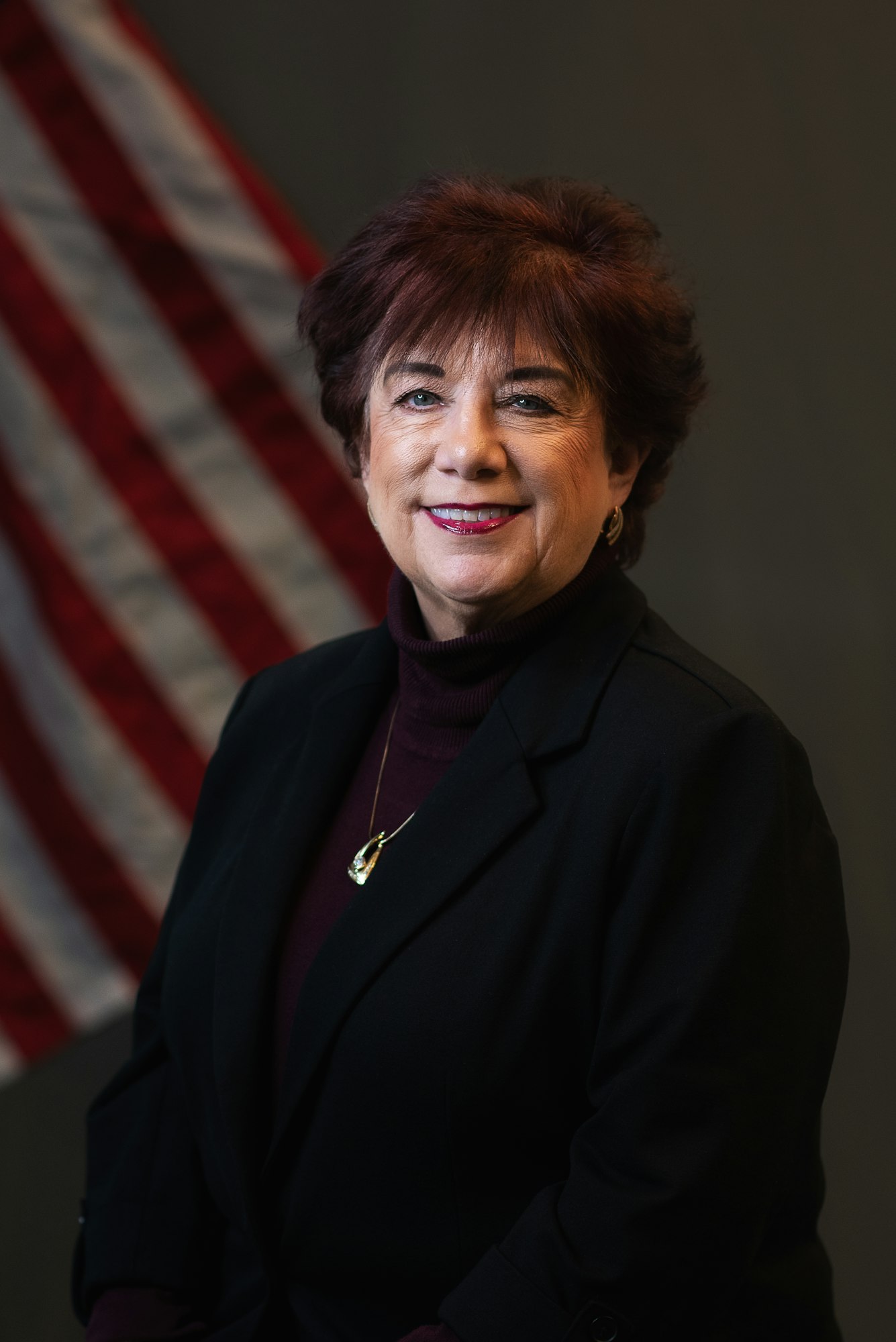 A person smiling in front of a U.S. flag background.
