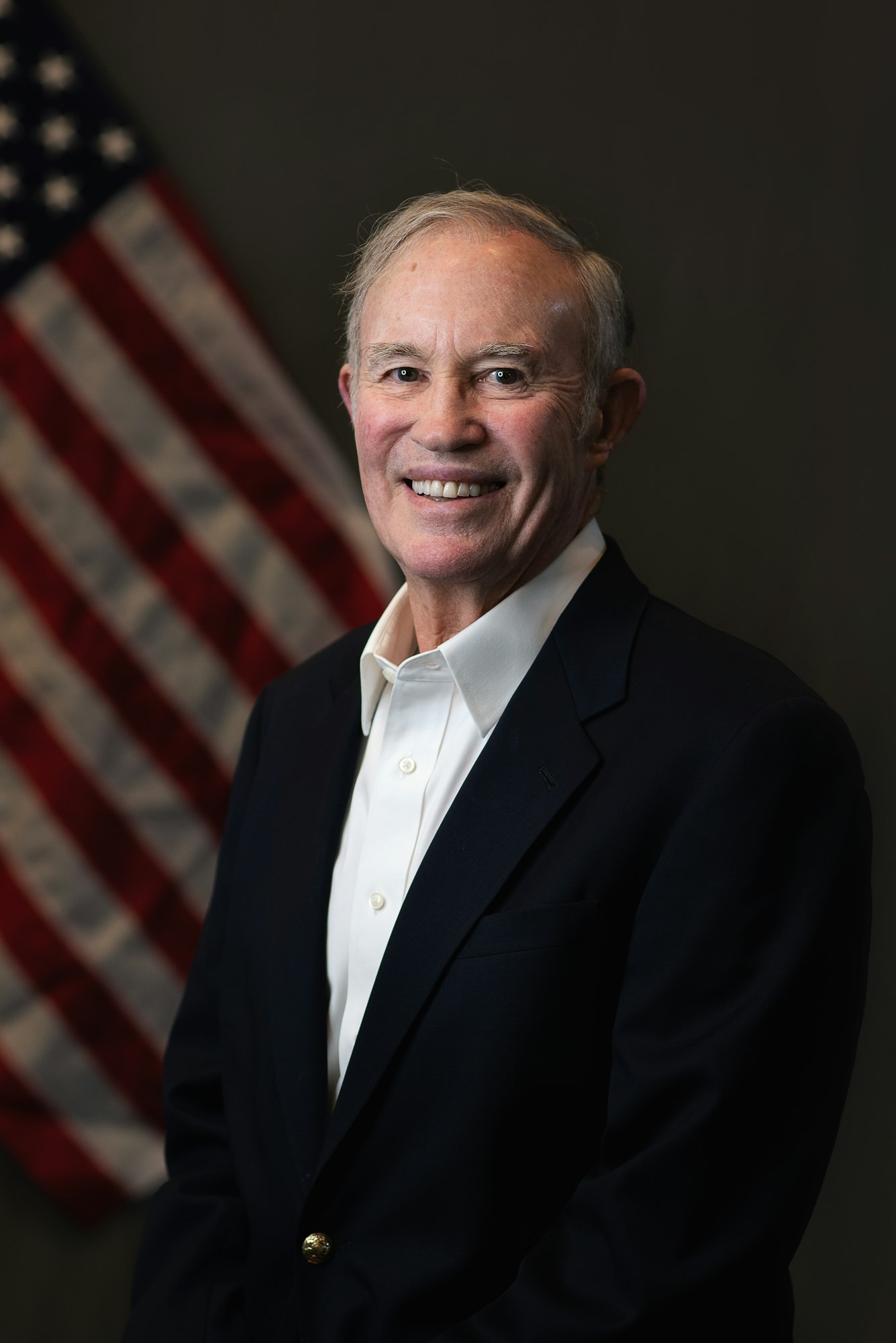 Smiling man in a suit with an American flag in the background.