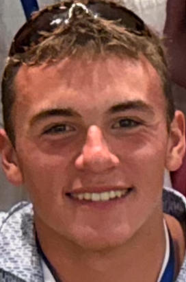 The image shows a young man smiling, wearing a jacket and sunglasses on his head, with a casual and friendly expression.