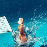 A person diving or splashing into a pool, legs up, near a diving board.