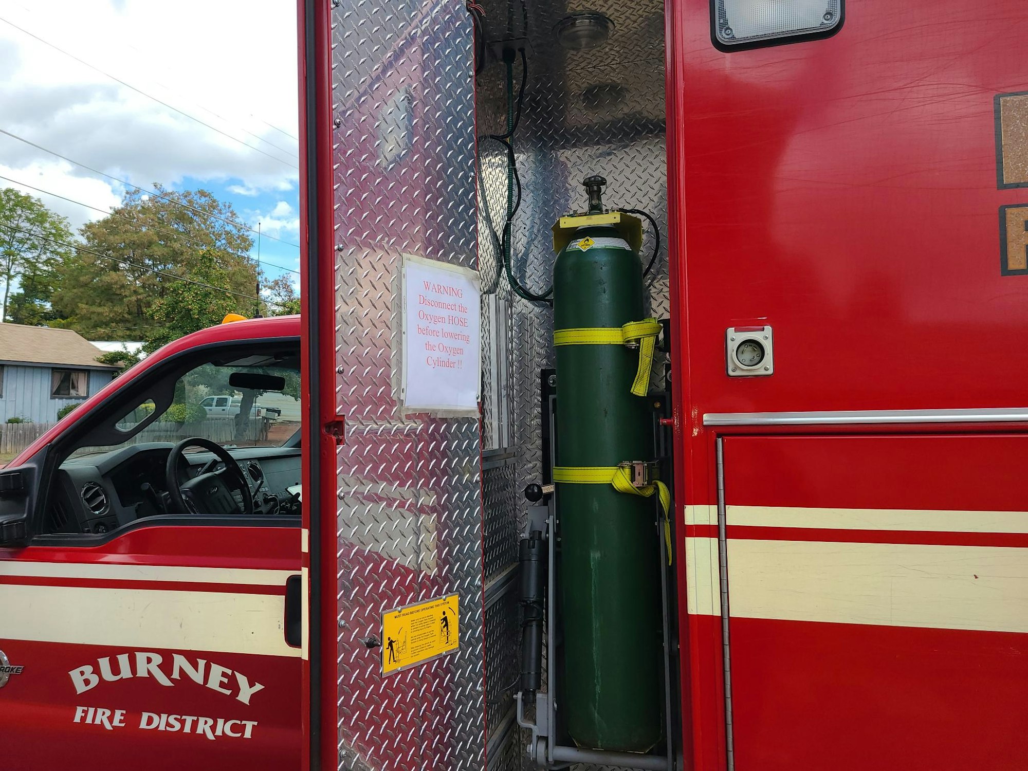 A red fire truck from "Burney Fire District" with an oxygen tank and a warning sign to disconnect the hose before taking out the tank.