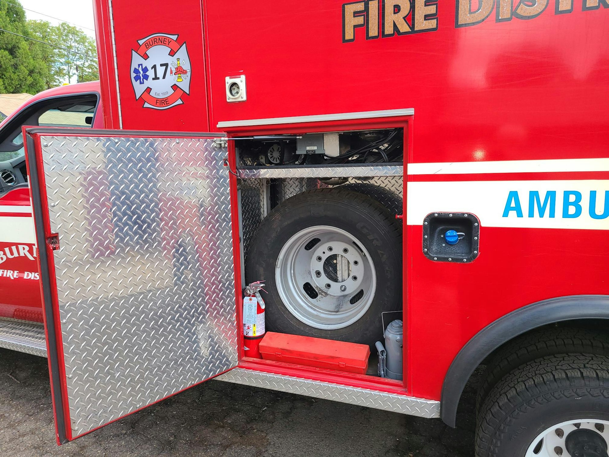 Red fire truck with an open compartment revealing a spare tire and a fire extinguisher.