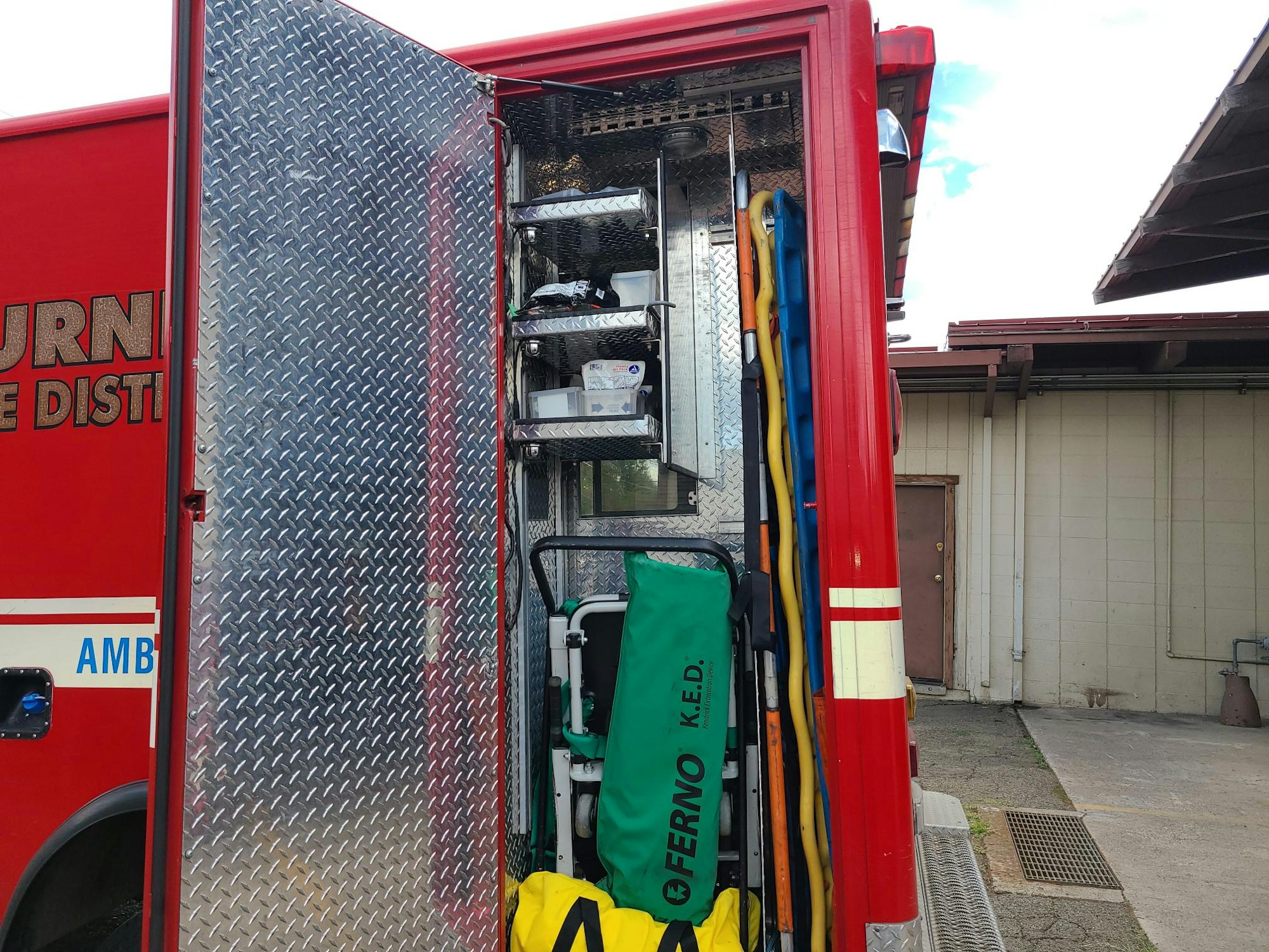 Open compartment on a fire truck with equipment like hoses, a stretcher, and emergency medical supplies.