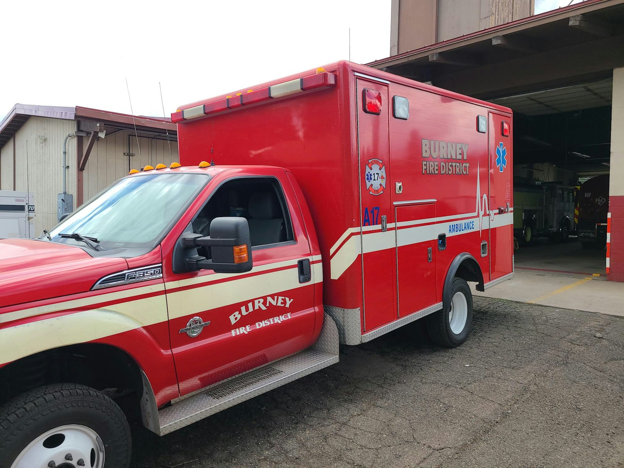 A red ambulance with "Burney Fire District" written on it, parked near a garage bay.