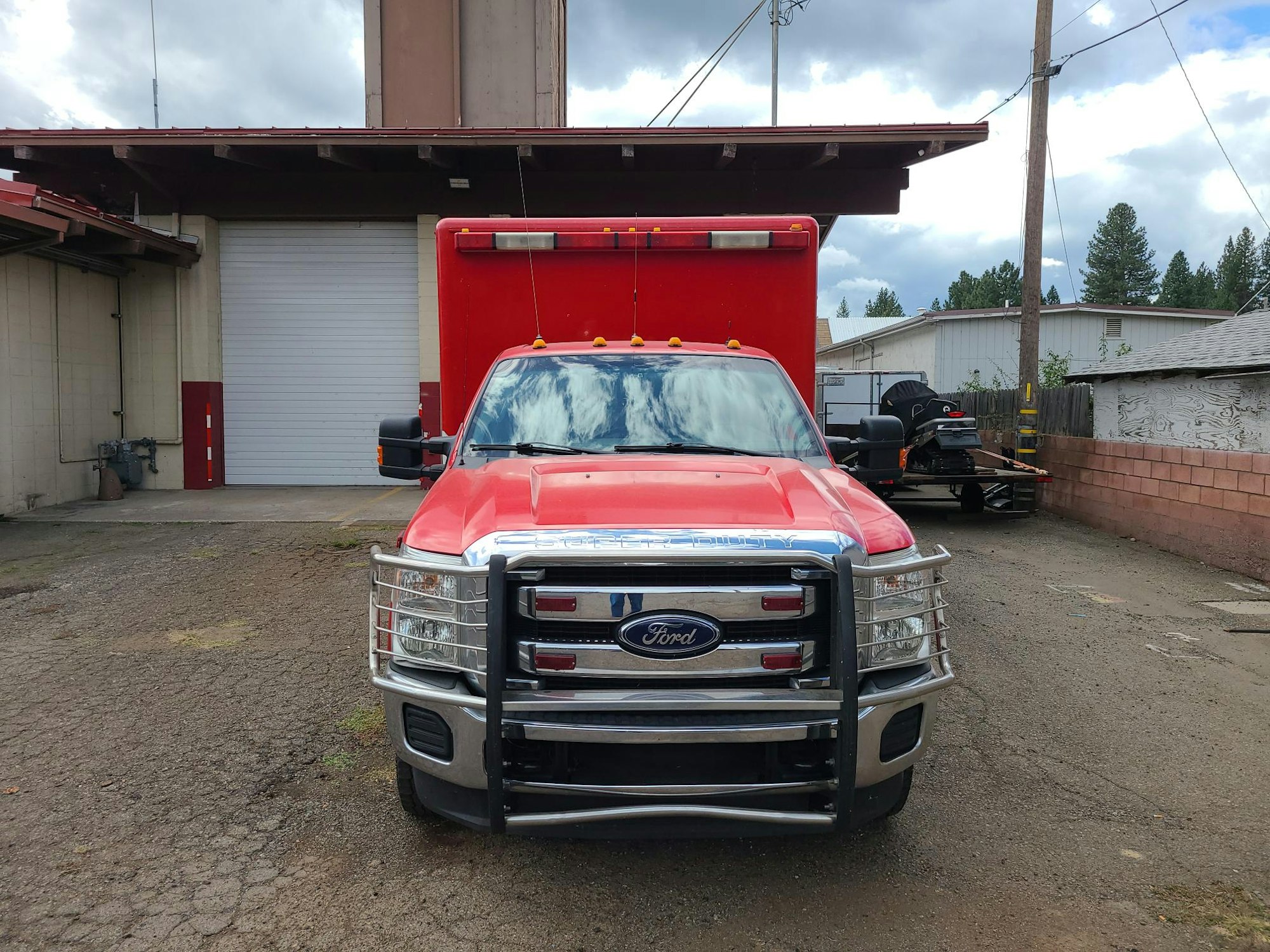 A red Ford truck parked in front of a fire station garage door, with overcast skies.