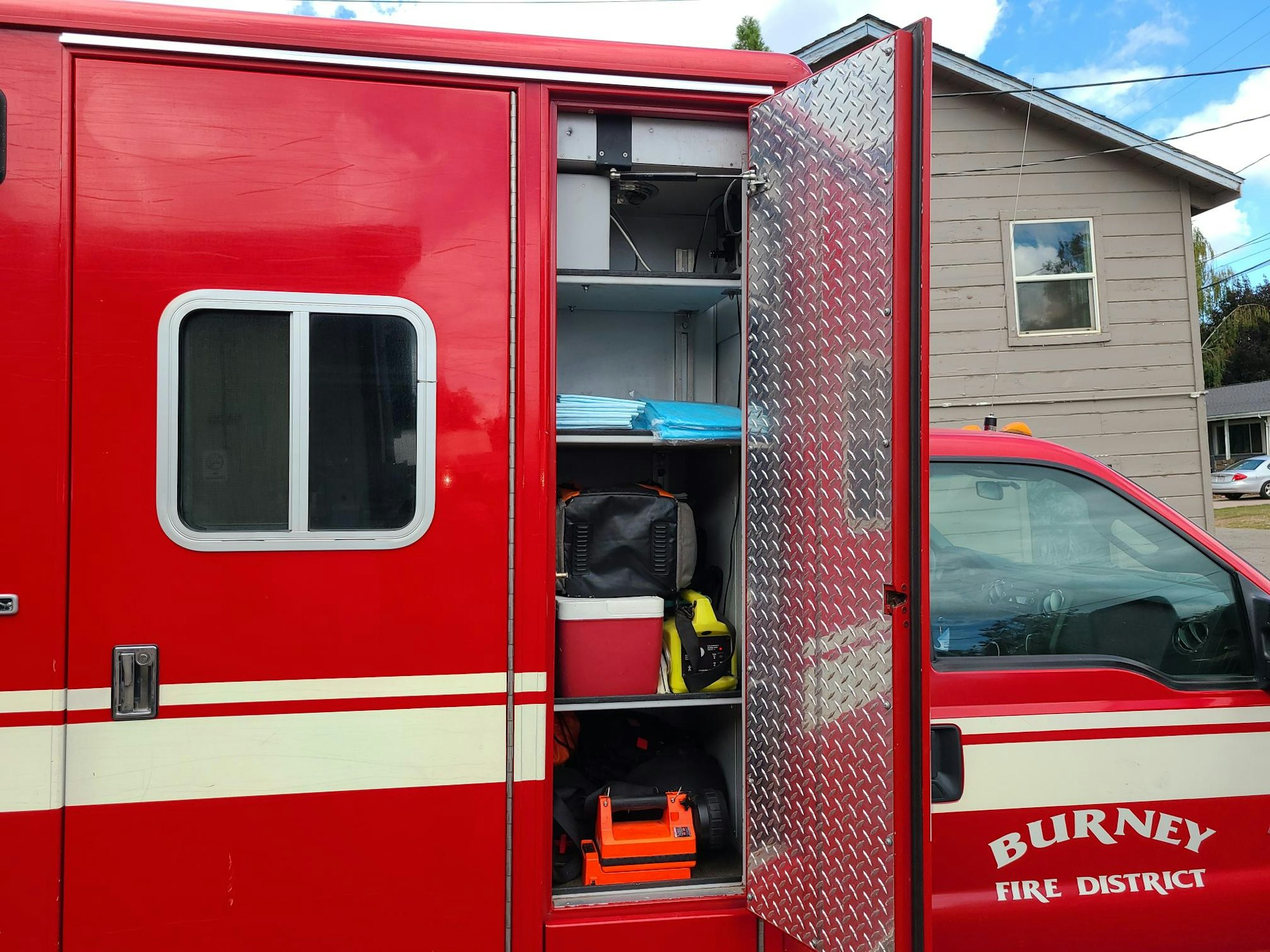 Side view of a red fire truck with storage compartment open, revealing equipment inside.
