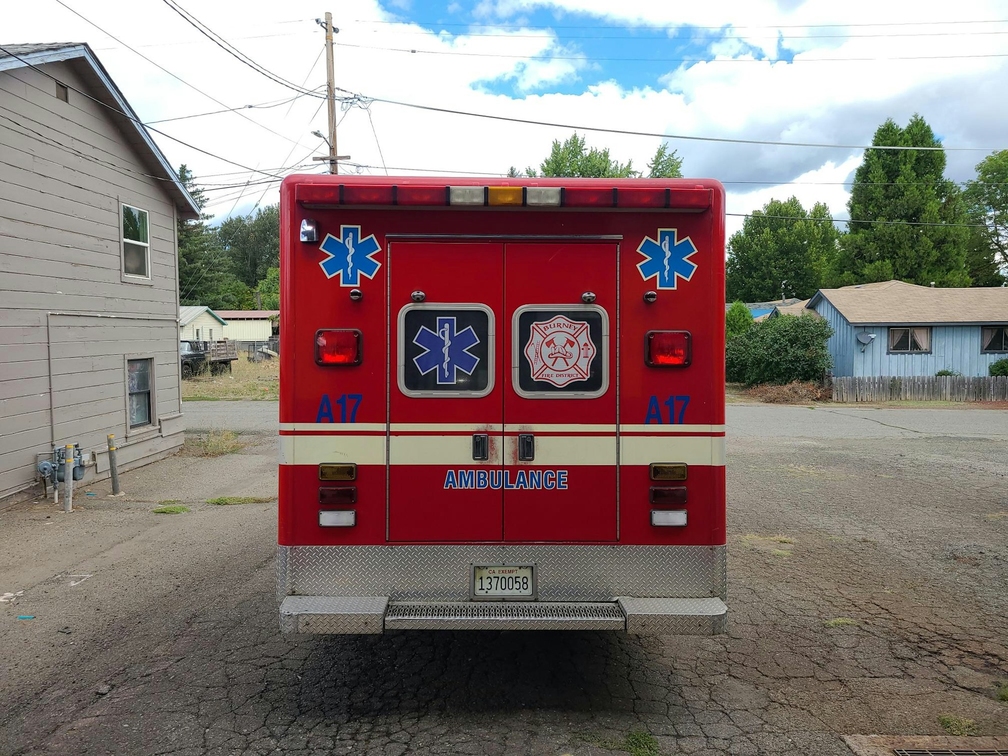 Rear view of a red ambulance with markings and emergency symbols, parked on a street.