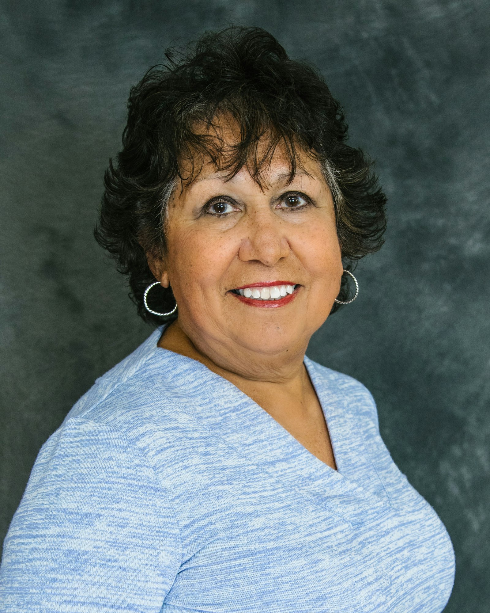 The image features a smiling woman with curly hair, wearing a blue top and hoop earrings, against a neutral background.