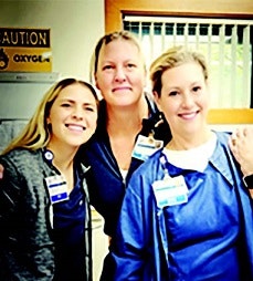 Three smiling healthcare workers in scrubs with ID badges in a hospital setting.