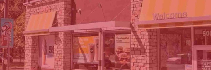 A fast-food restaurant exterior with promotional posters for ice cream and breakfast items under a welcome sign.