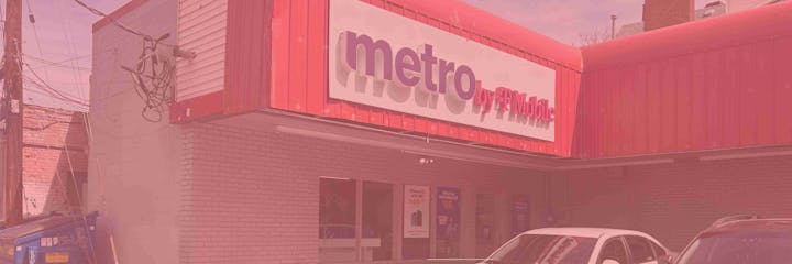 A Metro by T-Mobile store exterior with parked cars and promotional signs in the windows.