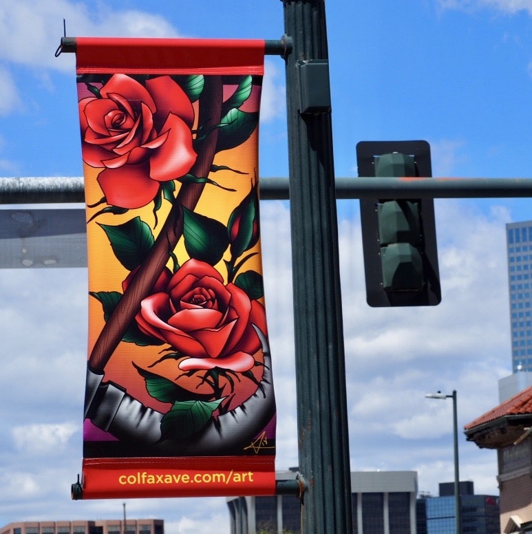 A street banner with red roses and green leaves against an orange background, featuring a website URL at the bottom.