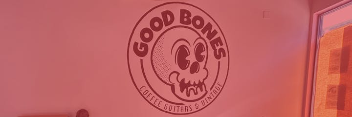 The image features a wall logo for "Good Bones," emphasizing coffee, guitars, and vintage items, with a playful skull design.