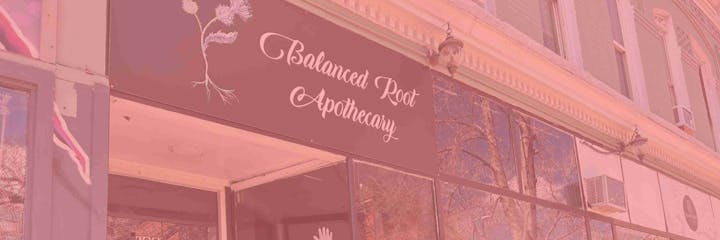 Storefront of "Balanced Root Apothecary" with sign and window reflections.