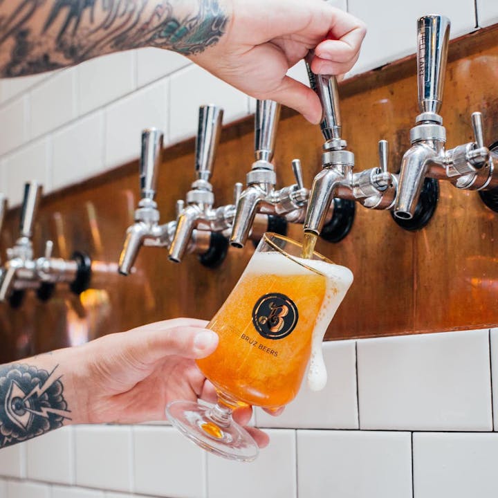 Tattooed arm pouring beer from a tap into a glass labeled "Bruz Beers."