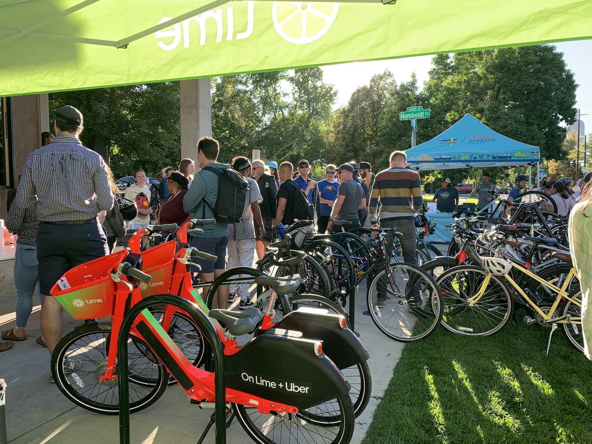 A group of people with bicycles gather under tents, featuring Lime and Uber bikes in the foreground.
