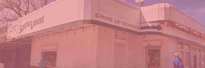 A liquor store with a drive-up service sign, and a person standing outside.