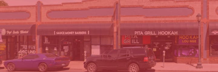 Storefronts including a barbershop, a pita grill, and a hookah lounge with cars parked in front.