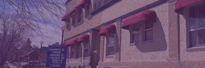 A building with red awnings, trees, and a sign for a Chinese medicine school in Colorado.