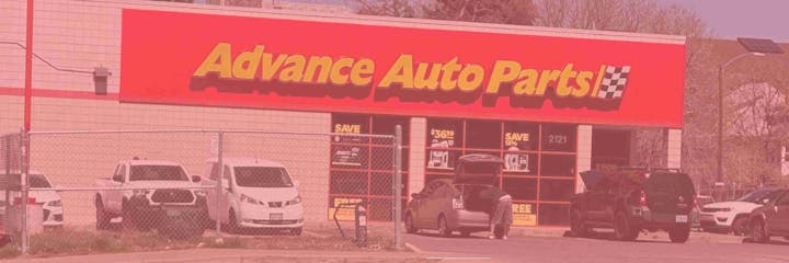 A store named "Advance Auto Parts" with cars parked in front and a person at an open trunk.