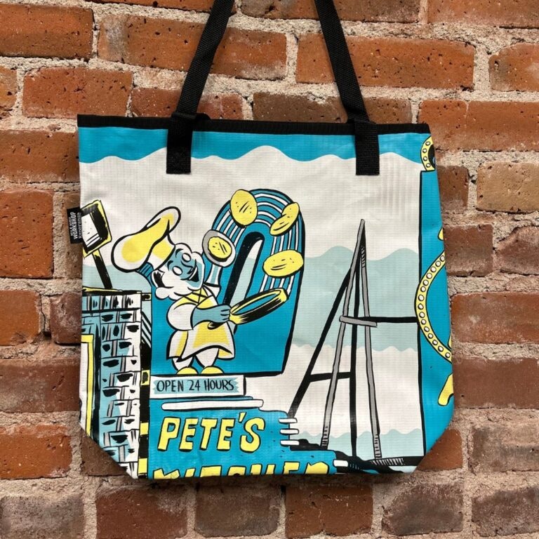 Tote bag with colorful illustration of a chef, pancakes, text "Pete's," and a bridge against a brick wall.