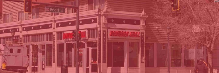 An urban street corner featuring "Bourbon Grill," traffic lights, a street sign for Pearl St, and a person walking.