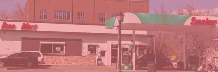 Gas station with "Sinclair" logo and "Dino Mart" next to it, parked cars, and people sitting nearby.