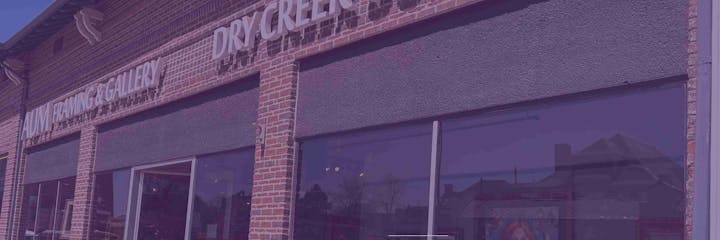 Brick storefront with signs for "AUM Framing & Gallery" and "Dry Creek." Black awnings and large windows.
