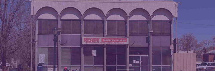 A building with "READY temporary services" sign, arched windows, trees, and parked bicycles.