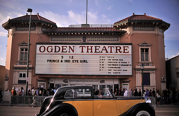 Ogden Theatre with a marquee listing events, a crowd, and a vintage car parked in front.