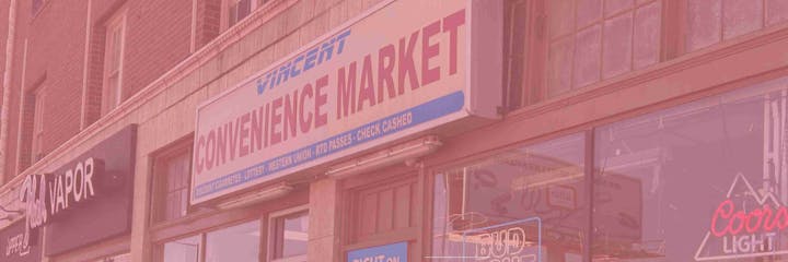 Building with signs for a convenience market and a vapor shop; window displays a neon Coors Light sign.