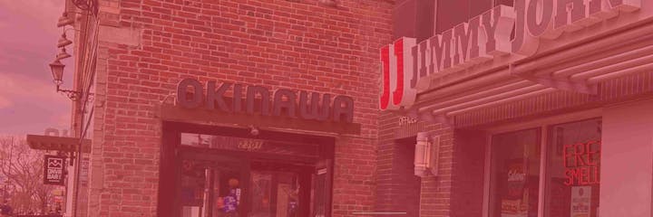 Brick storefronts with signs for "Okinawa" and "Jimmy John's," a lantern, and a "DNVR Bar" sign partially visible.