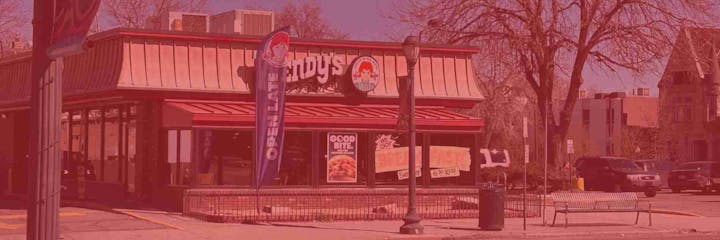 A fast-food restaurant with a red-themed exterior, including a banner reading "OPEN LATE," parked cars, and a bench out front.