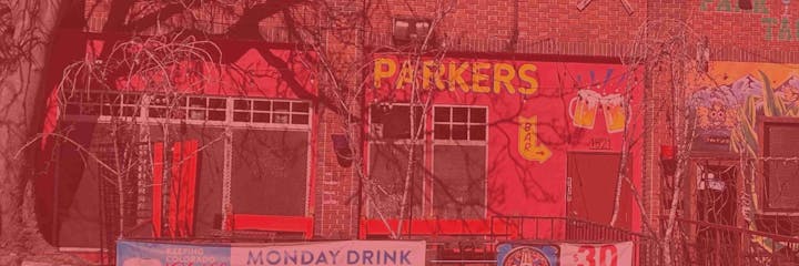 A red brick building with "PARKERS BAR" sign, beer mug graphics, and outdoor seating.