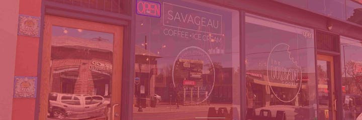 Storefront of Savageau Coffee & Ice Cream with "OPEN" sign, reflecting street and urban scenery.